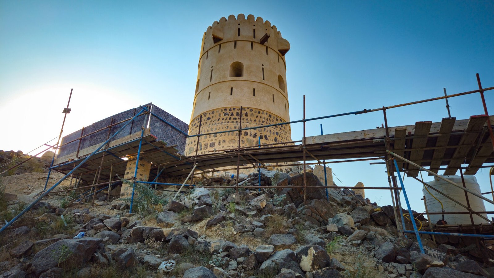 Traditional-style watchtower surrounded by construction scaffolding and building materials during restoration work on mountain hilltop.